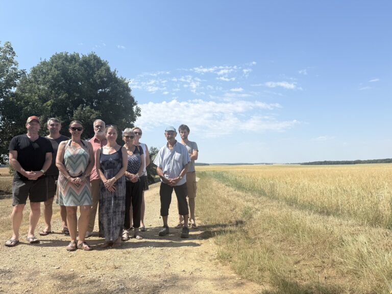 Neuf membres de l'association Stop Éoliennes réunis sur un chemin agricole, devant un champ de blé et l'horizon boisé de Nesle-et-Massoult.